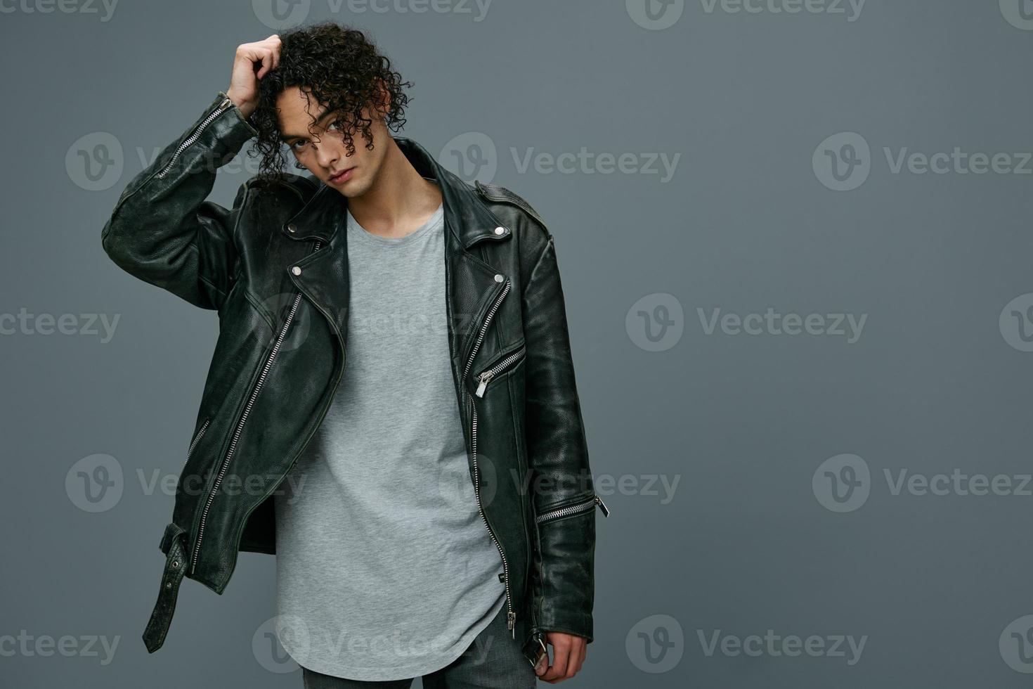 Cool fashion offer. Pretty stylish tanned curly man leather jacket looks at camera posing isolated on over gray studio background. Huge Seasonal Sale New Collection concept. Copy space for ad photo