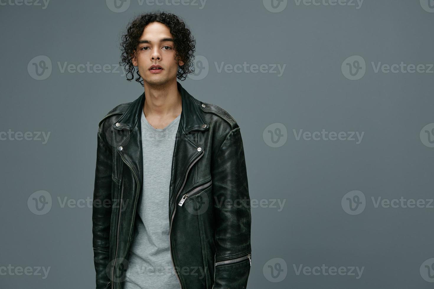 Cool fashion offer. Pretty stylish tanned curly man leather jacket looks at camera posing isolated on over gray studio background. Huge Seasonal Sale New Collection concept. Copy space for ad photo
