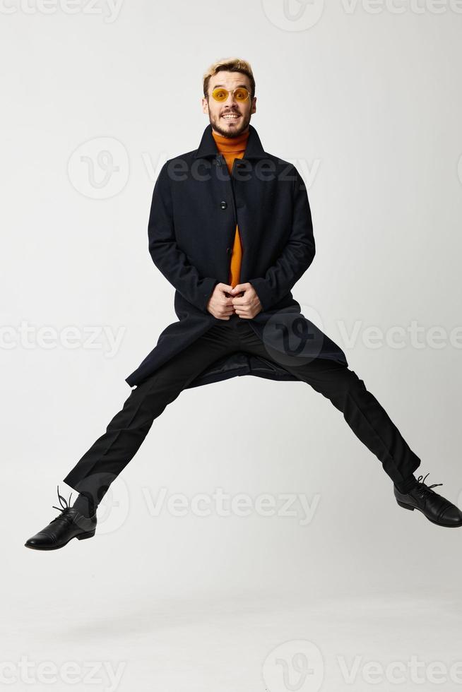 fashionable man in black coat jumped up with legs apart and orange sweater Copy Space photo