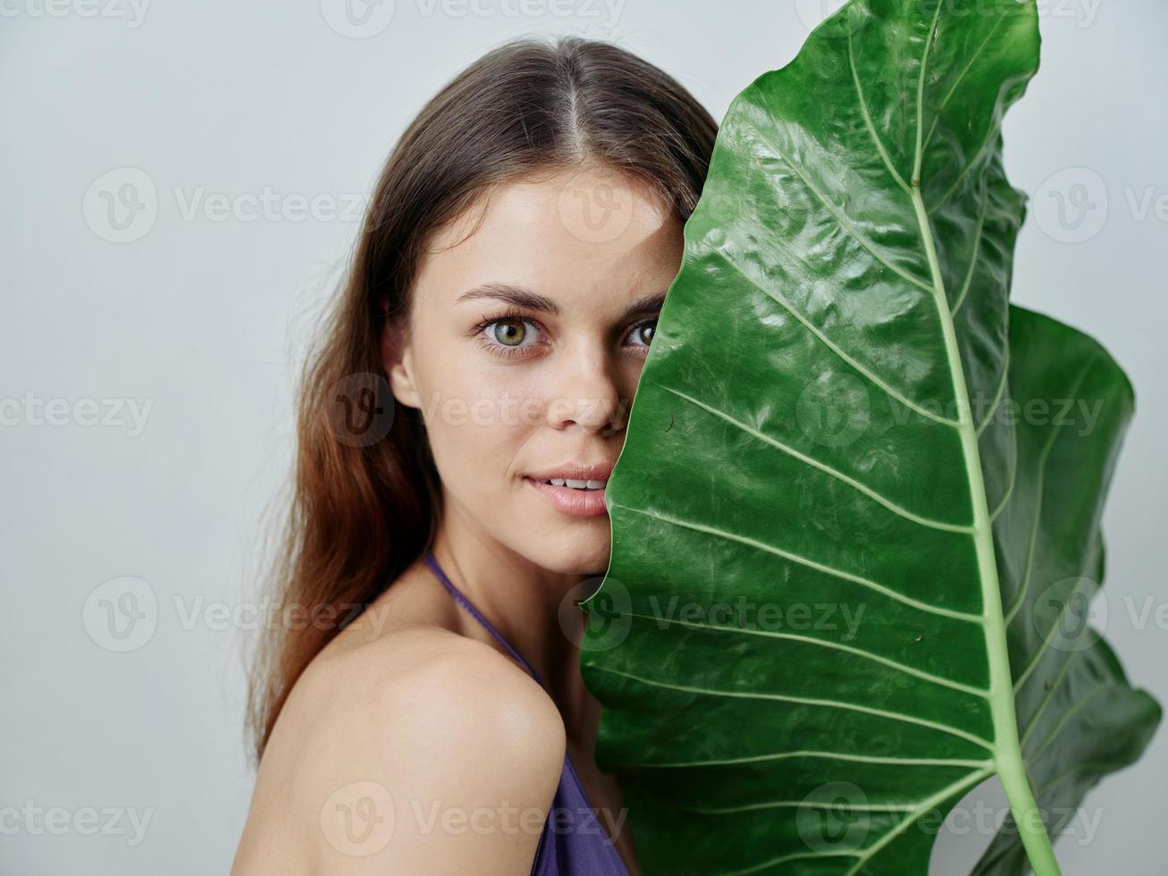 mujer participación un verde grande hoja cerca su cara atractivo Mira desnudo espalda de cerca foto