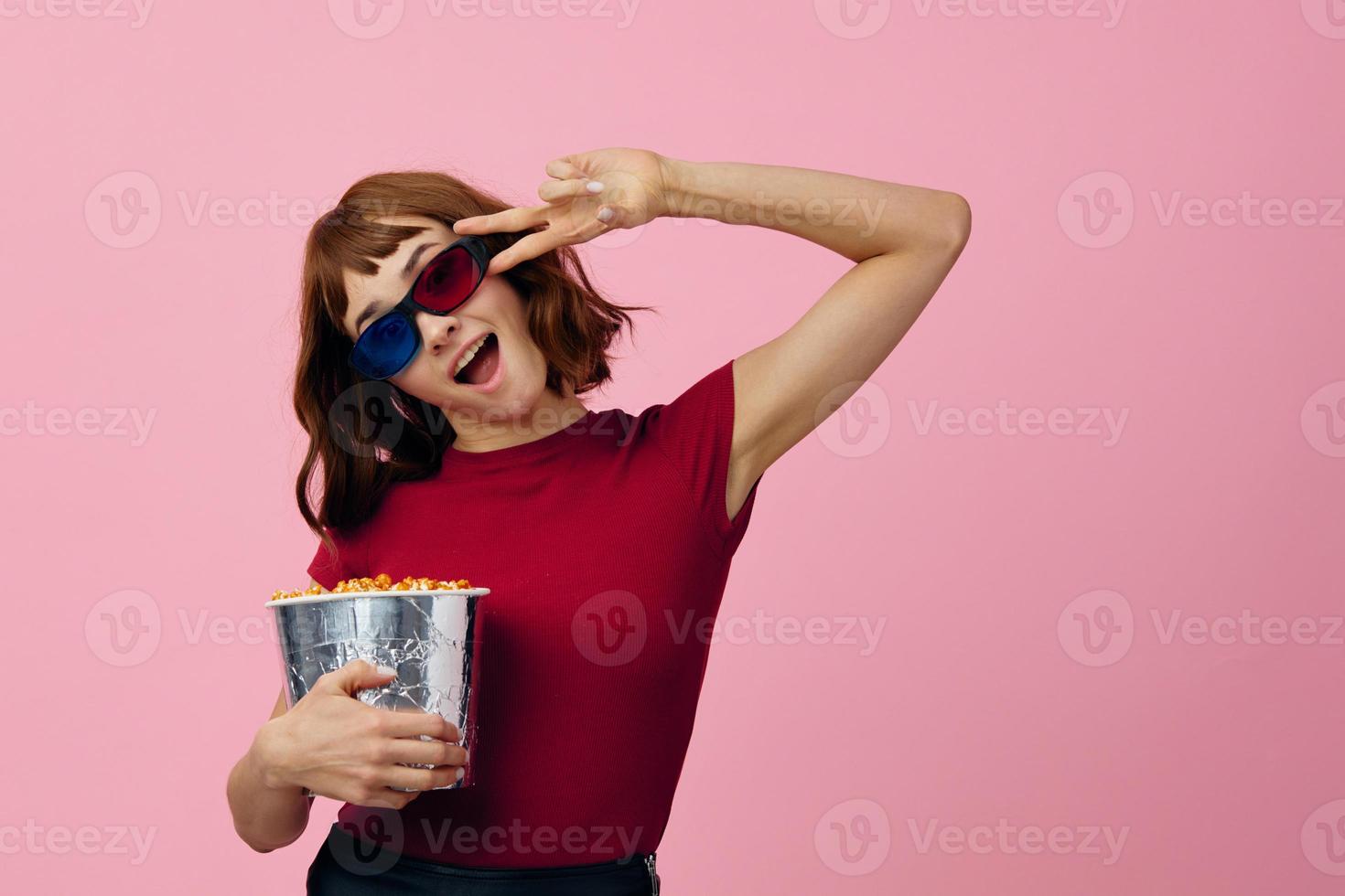 Overjoyed happy cute redhead lady in red t-shirt 3D glasses with popcorn watch movie posing isolated on over pink studio background. Copy space Banner. Fashion Cinema concept. Entertainment offer photo