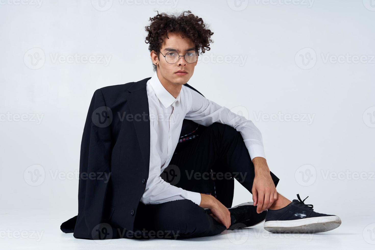 stylish man with curly hair in sneakers on a light background a jacket on the shoulder pants model photo