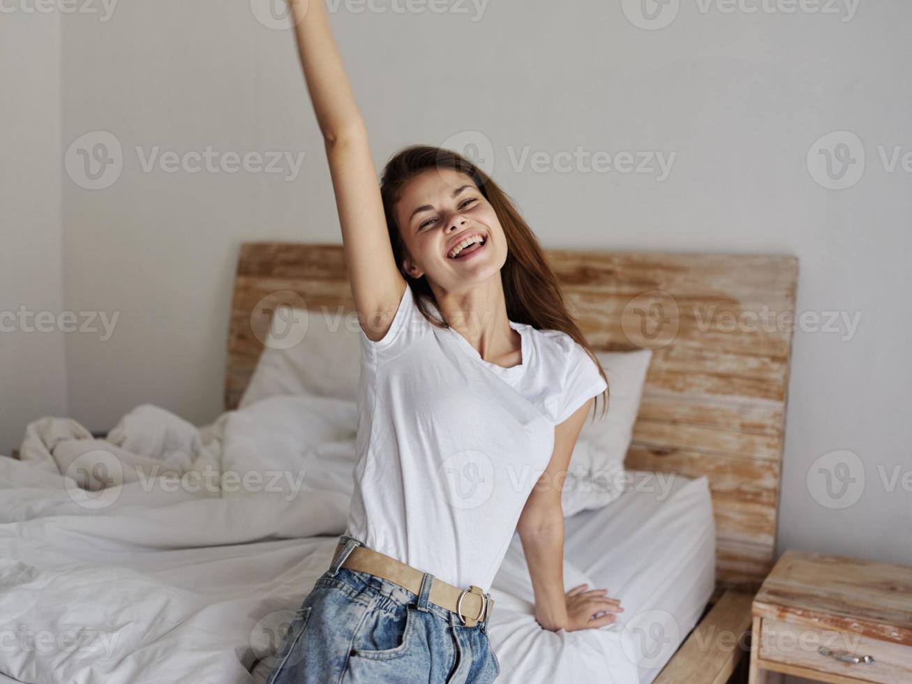 young woman sitting on bed indoors with hand raised up interior photo