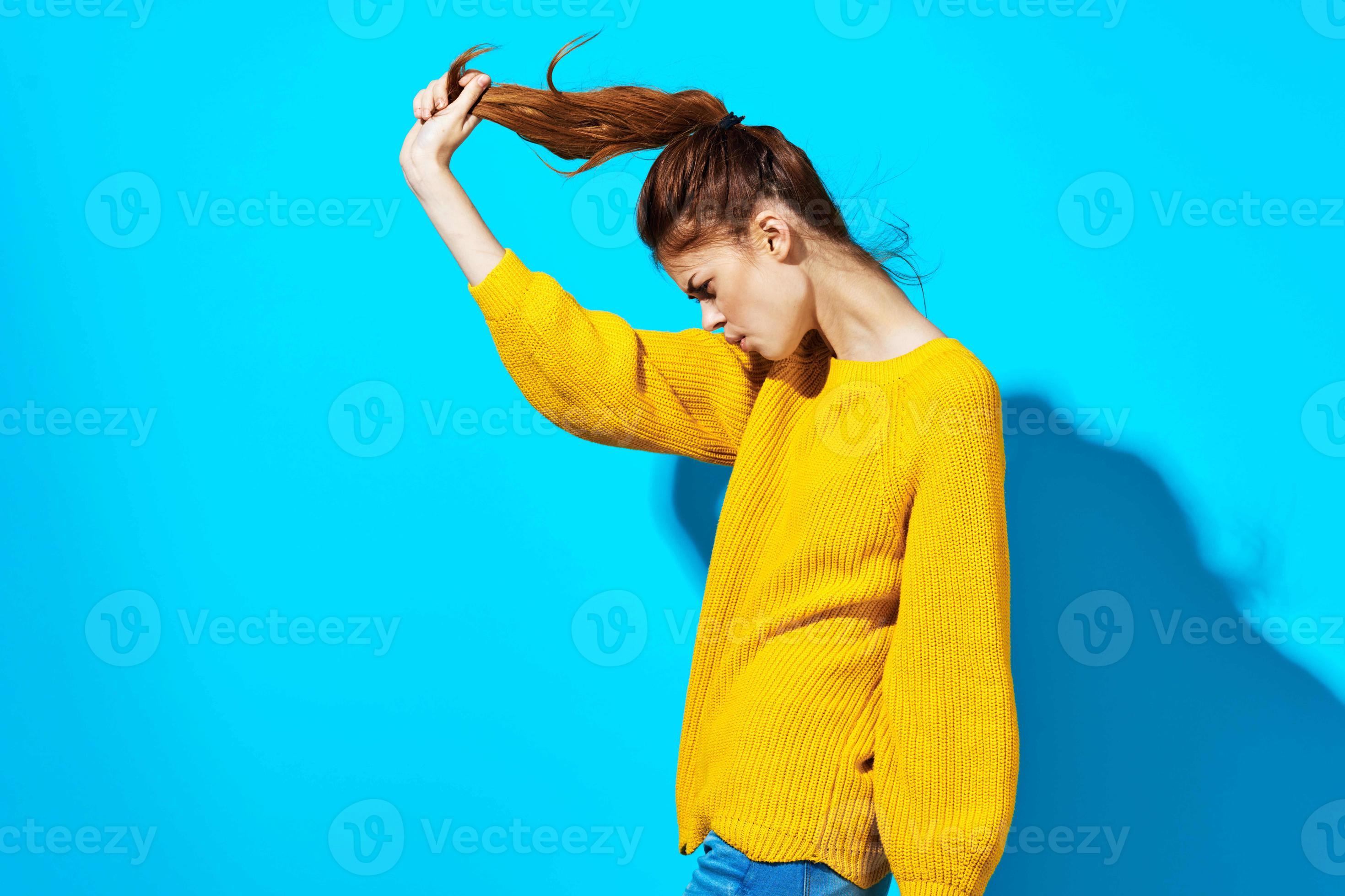 woman in yellow sweater holding hair blue background fashion 22072636