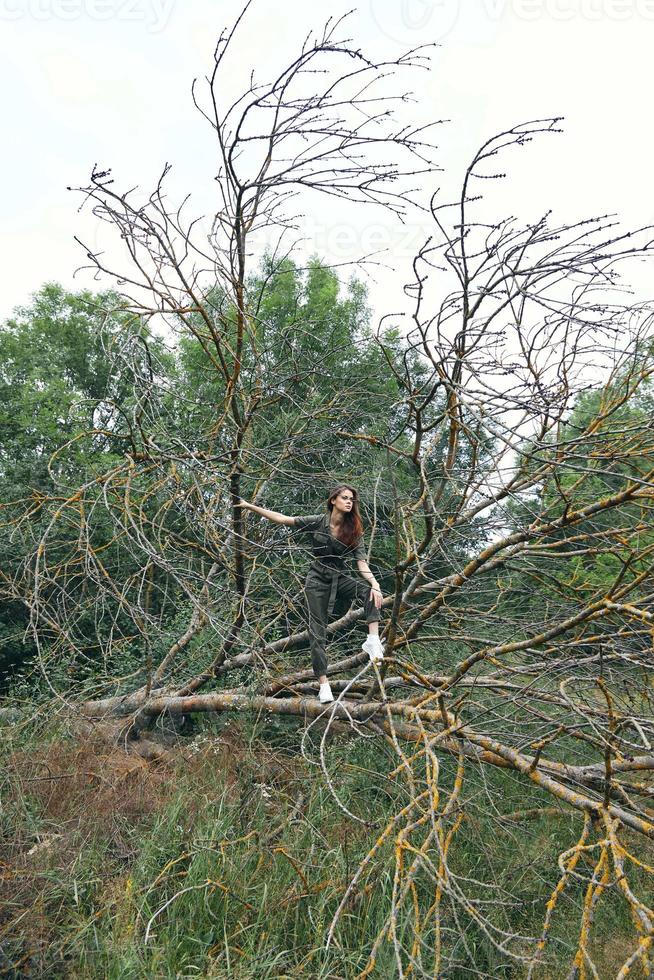 woman in sneakers is standing on a broken tree in the forest and wearing a green jumpsuit photo