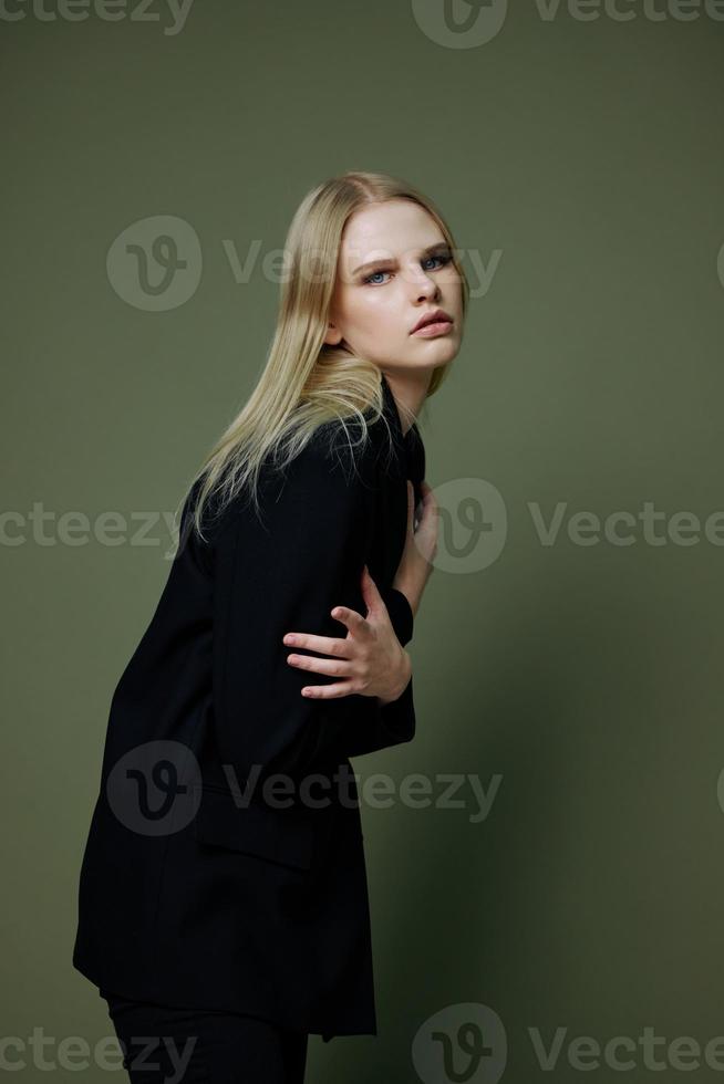 Art fashion photo shoot. Professional blonde model holds herself hugs with both hands half-turned looks at the camera posing on a green background in the studio