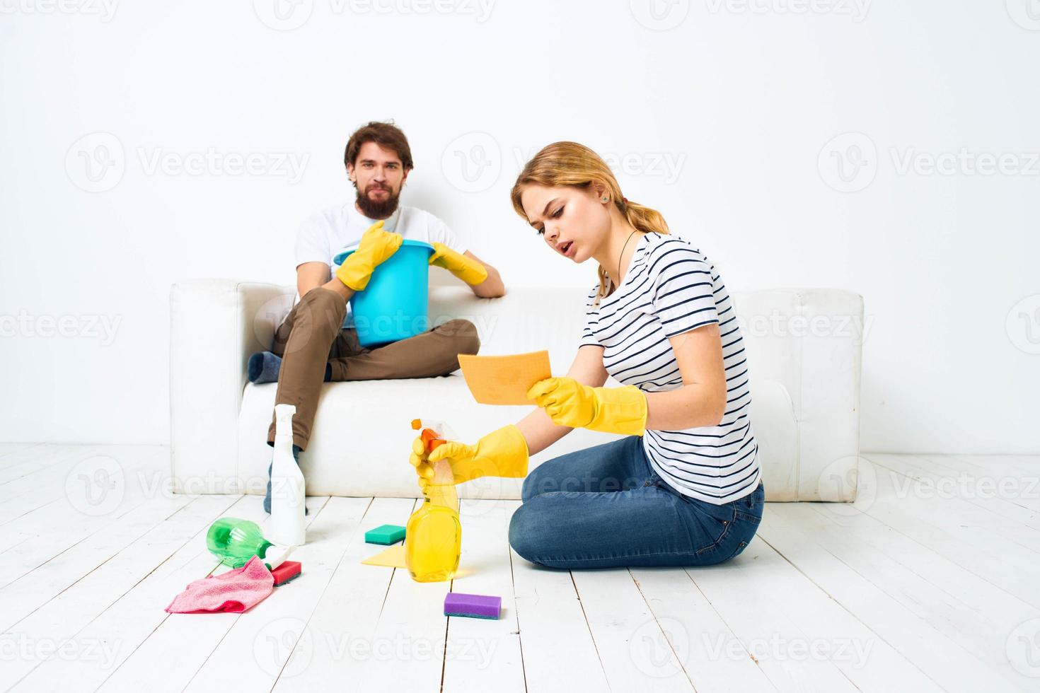 A man sits on a sofa with a bucket of a woman on the floor with a detergent for kitchen interior chores photo