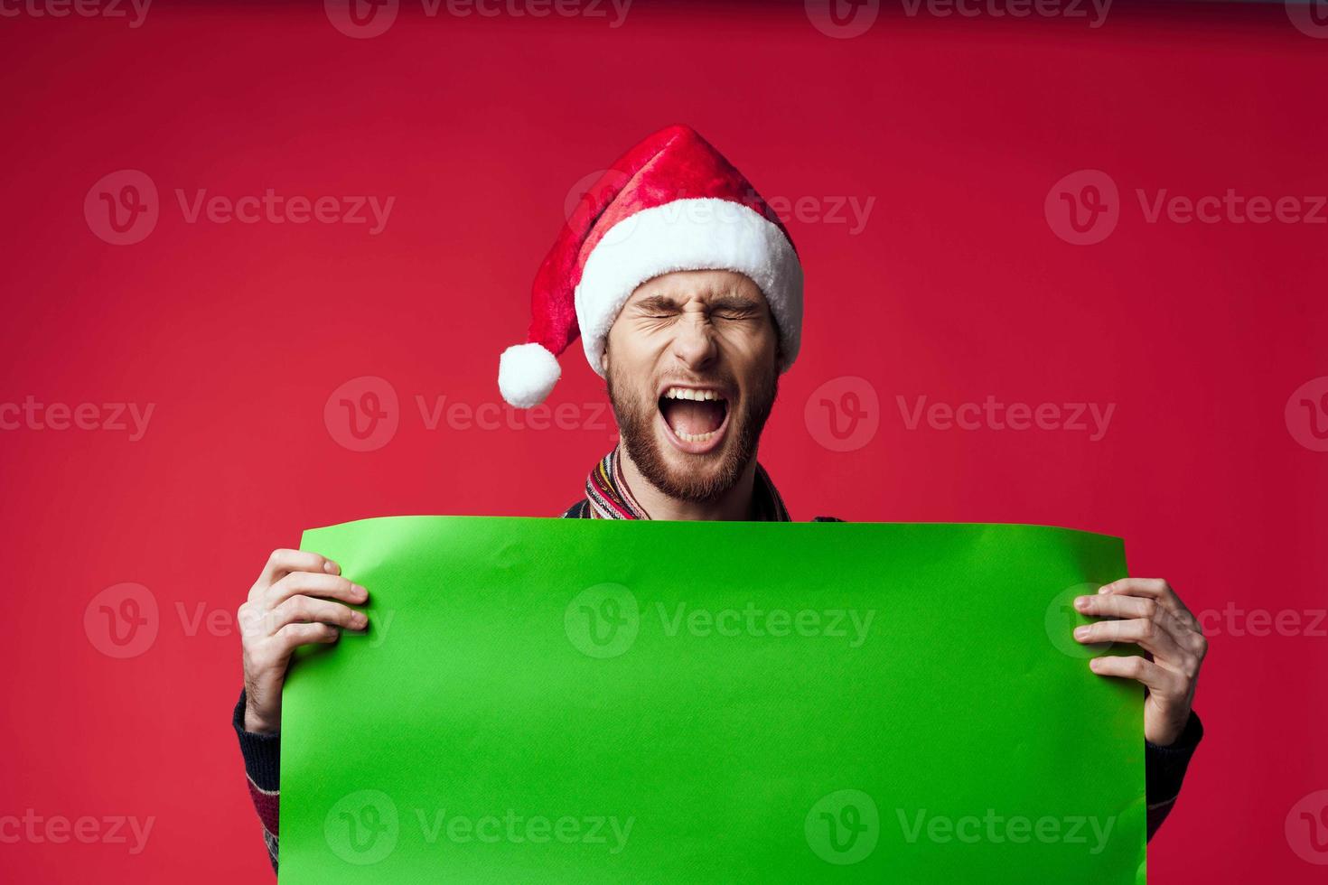 Cheerful man in a santa hat holding a banner holiday red background photo