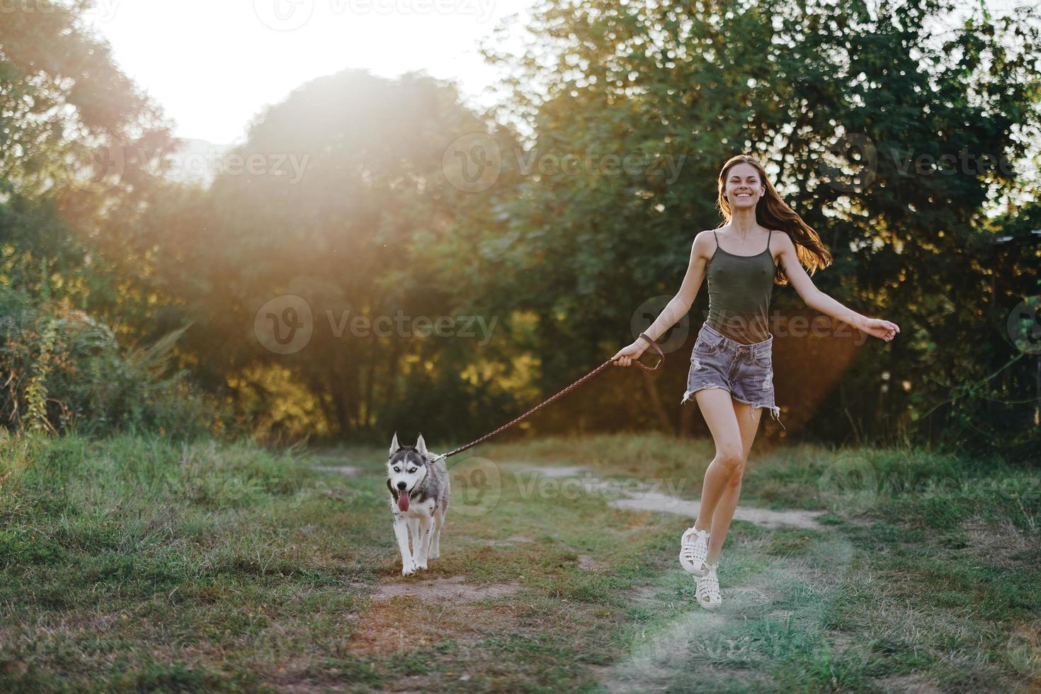 Woman and her husky dog happily running through the grass in nature in the park smile with teeth fall walk with pet, traveling with a dog friend photo