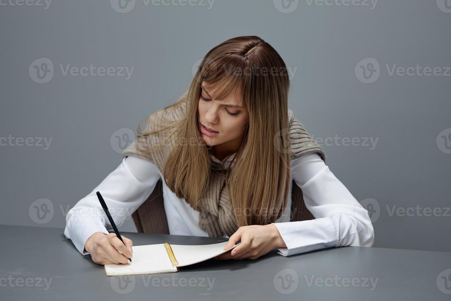 Angry irritated young blonde student lady freelancer in warm sweater hate doing home task at copybook in gray modern home office. Remote Job, Education And Career Profession Concept. Copy space photo