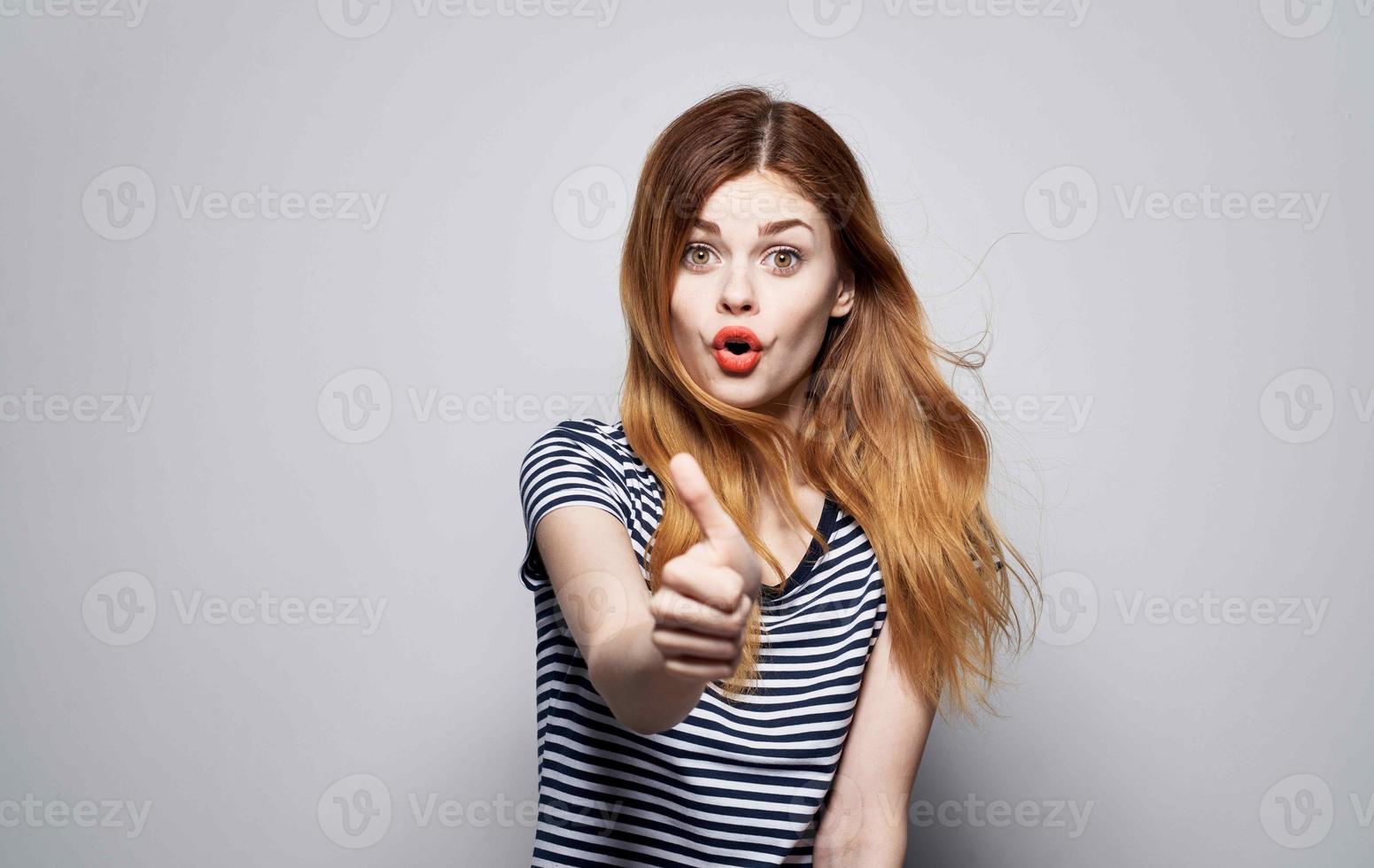 pretty woman in striped t-shirt throws up her hands emotions red lips studio photo