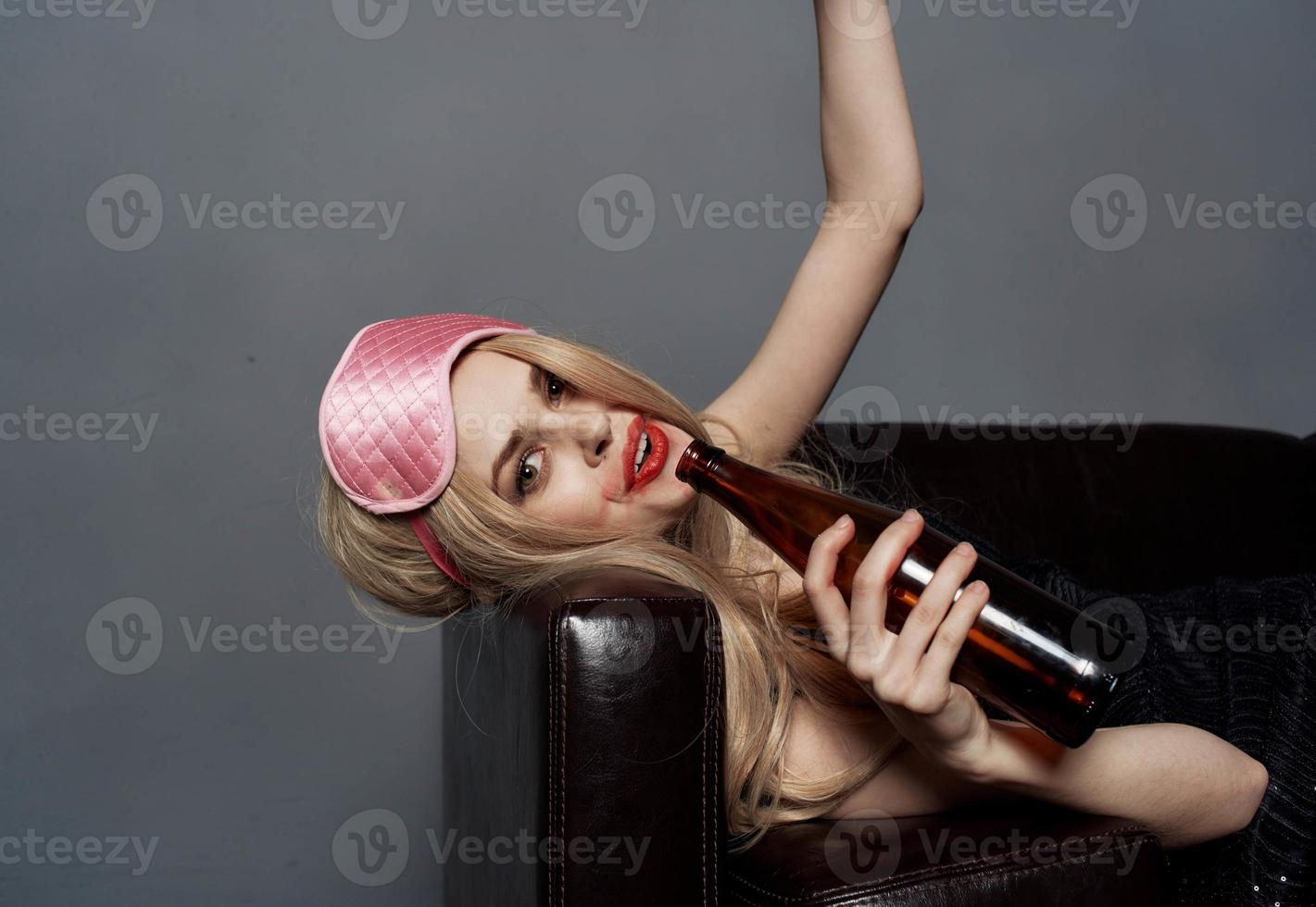 A drunk woman with a bottle of beer looks at a mobile phone in her hand and lies on the couch photo