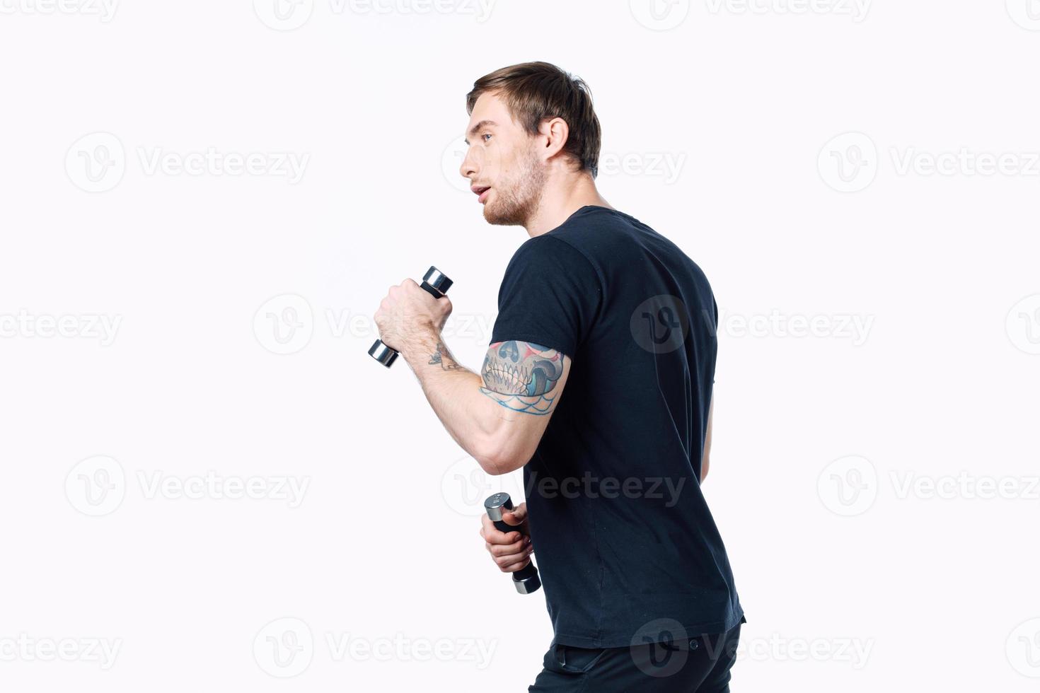 an athlete in a black T-shirt with dumbbells is engaged in fitness on a white background side view photo