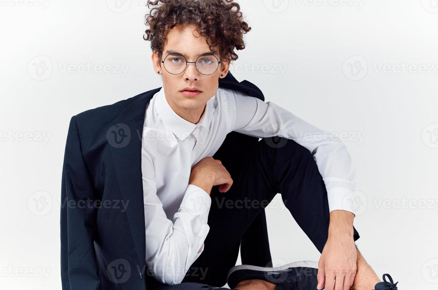 a guy in a classic suit and glasses sits on the floor In a bright room photo