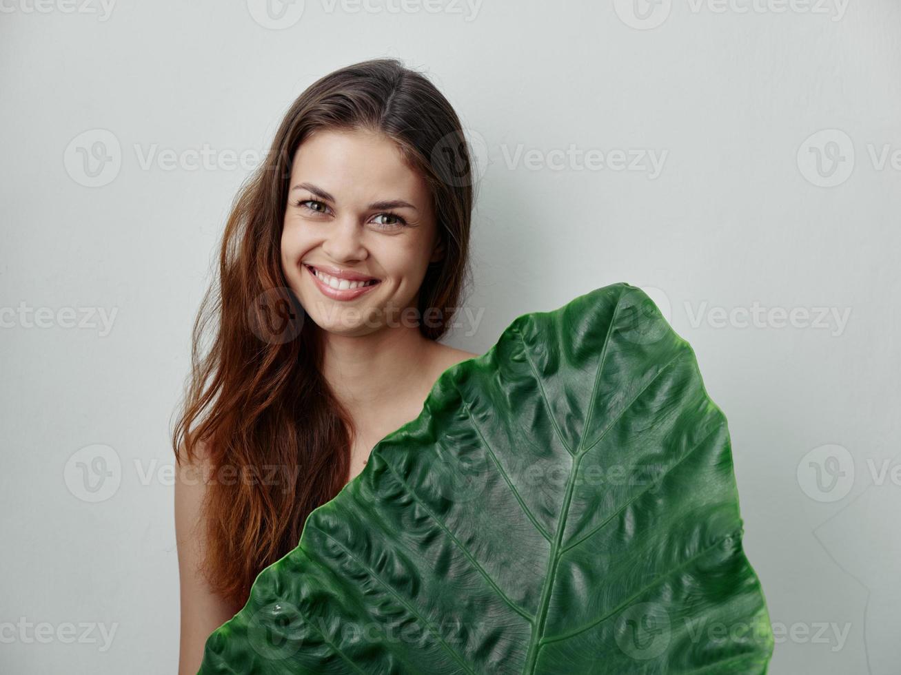 Cheerful red-haired woman covers naked body with palm leaf photo