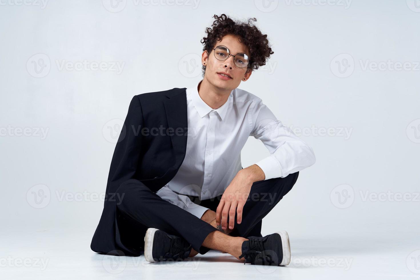 a guy in a shirt, trousers and sneakers on the floor in a bright room and a jacket on his shoulder photo
