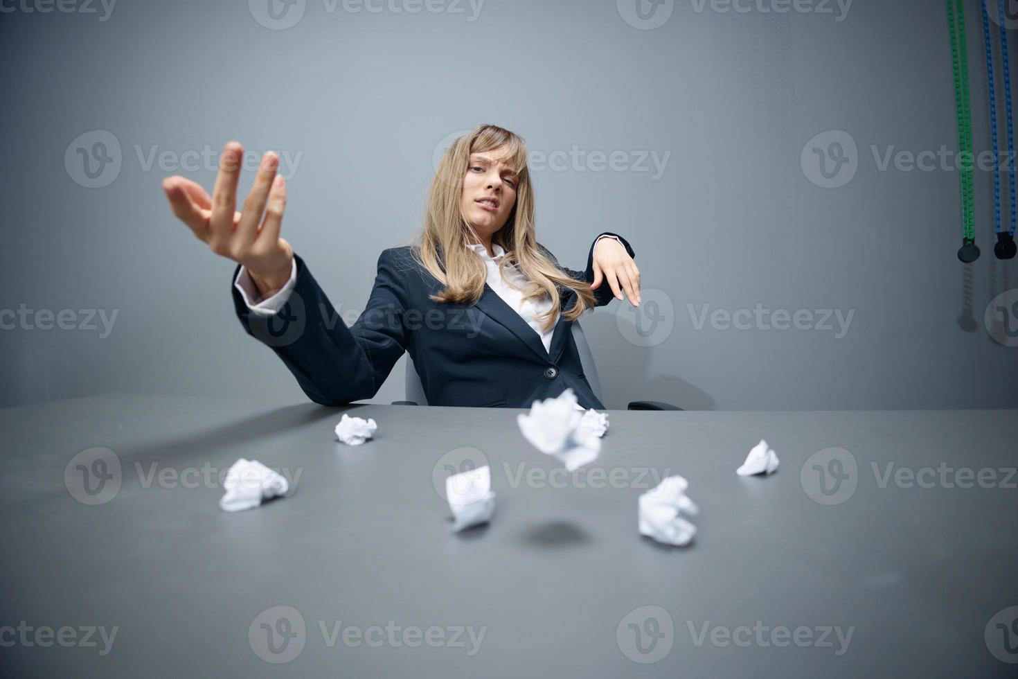 Pretty millennial blonde businesswoman worker in blue jacket throws papers into the camera sitting at workplace in gray modern office. Big boss Concept. Copy space, wide angle photo