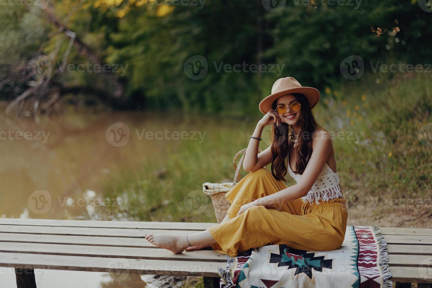 Woman in hippie eco clothing sits outdoors in the fall by the lake on a bridge resting and admiring the scenery watching the sunset photo