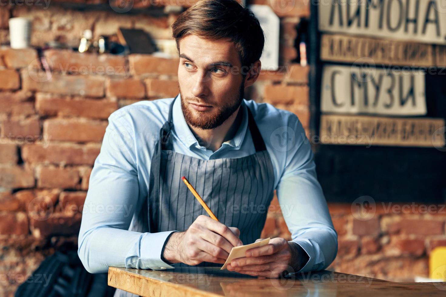 a man in an apron sits at a table accepting an order a cafe waiter photo