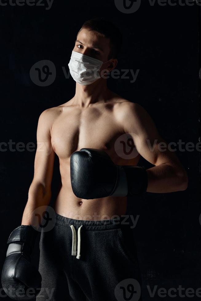 carrocero Boxer en un médico máscara en un negro antecedentes guantes atleta desnudo torso foto