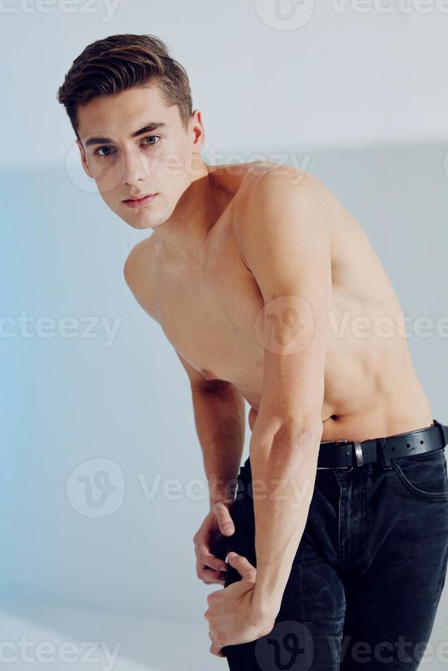Handsome young man in black pants on a light background and a naked torso photo