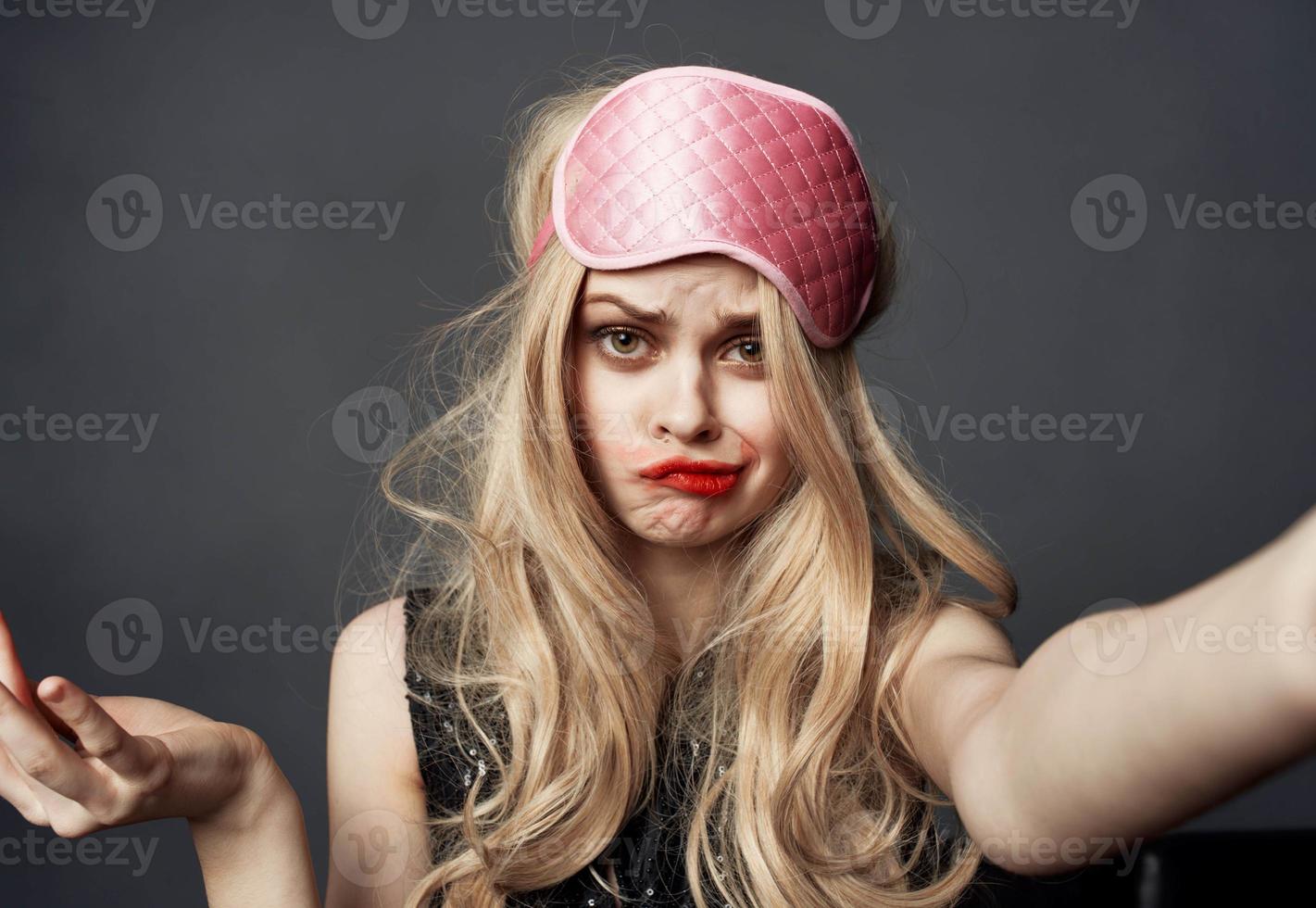A drunken blonde with a pink sleep mask on her head smears lipstick on her face photo
