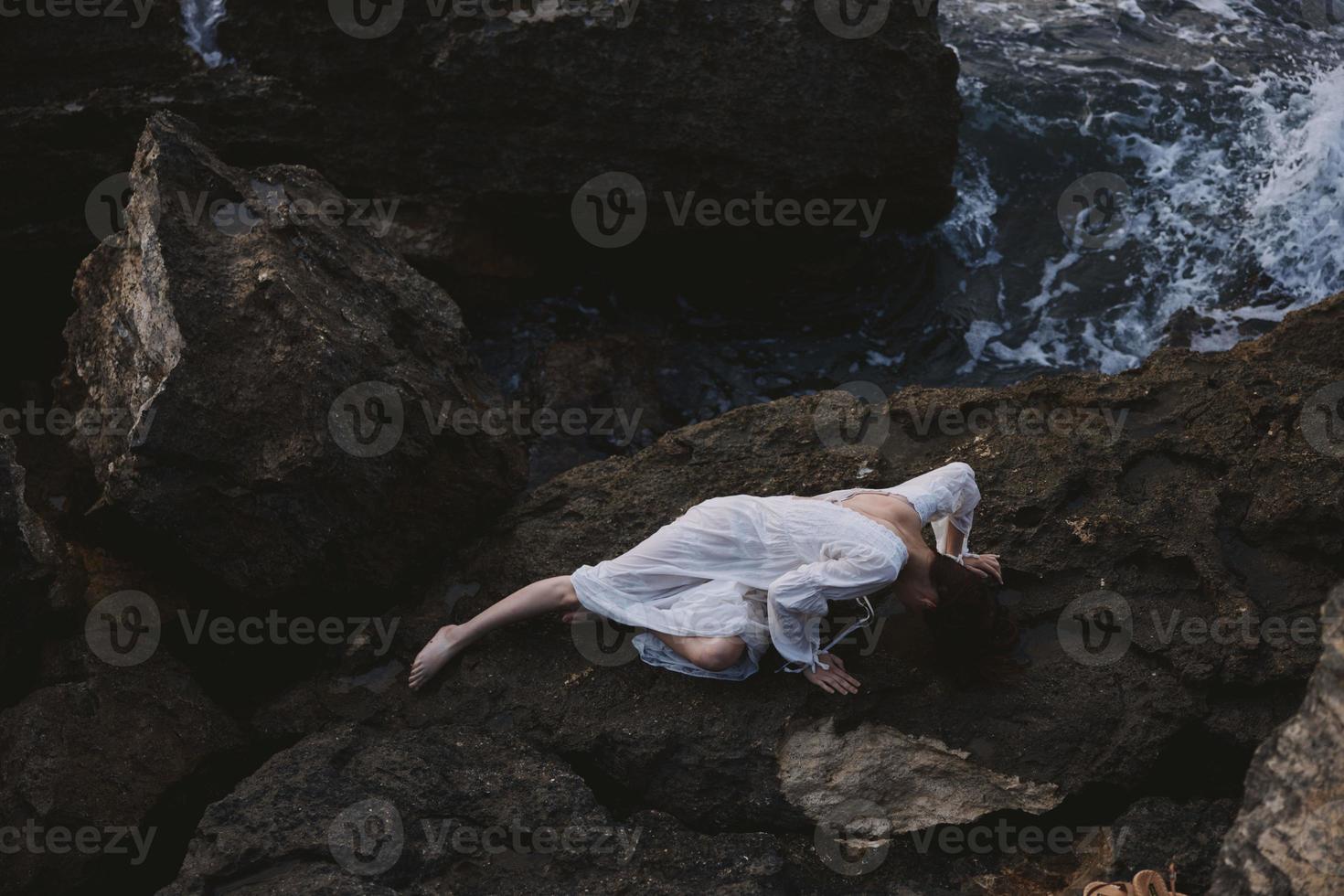 Beautiful bride lying on rocky coast with cracks on rocky surface landscape photo