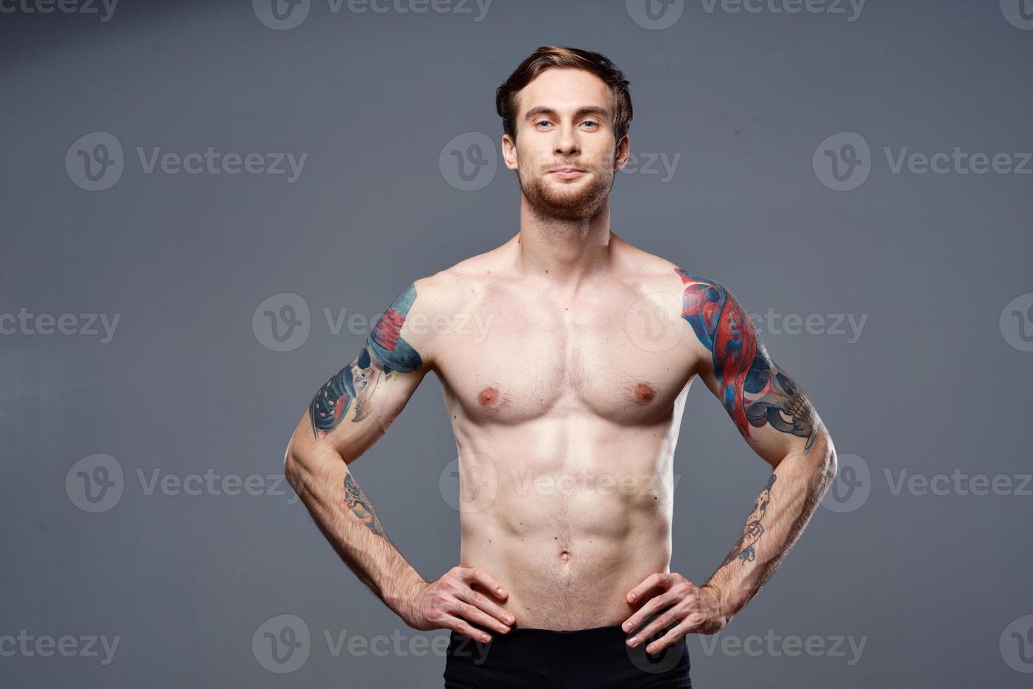 handsome man with a naked pumped-up torso tattoos on his arms holds his hands on his belt photo