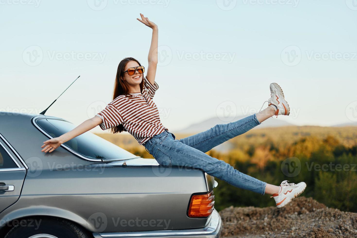 A woman with a car stopped on the road to rest on the journey raised her arms and legs from happiness and a beautiful landscape photo