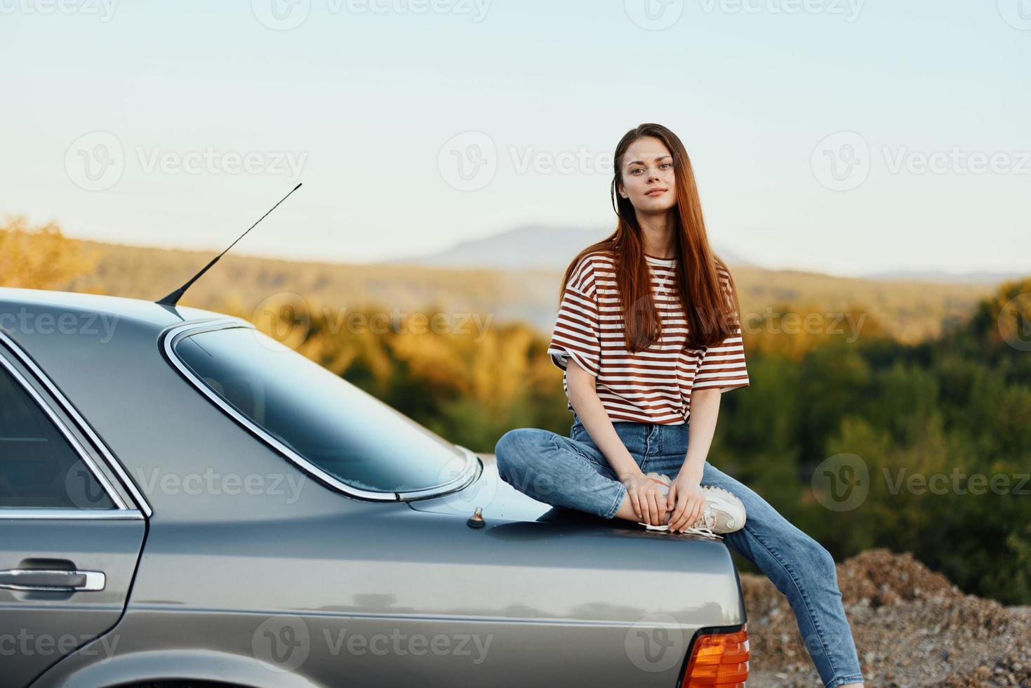 A woman car driver sits on the trunk of a car and looks into the distance admiring a beautiful view of autumn nature and mountains photo