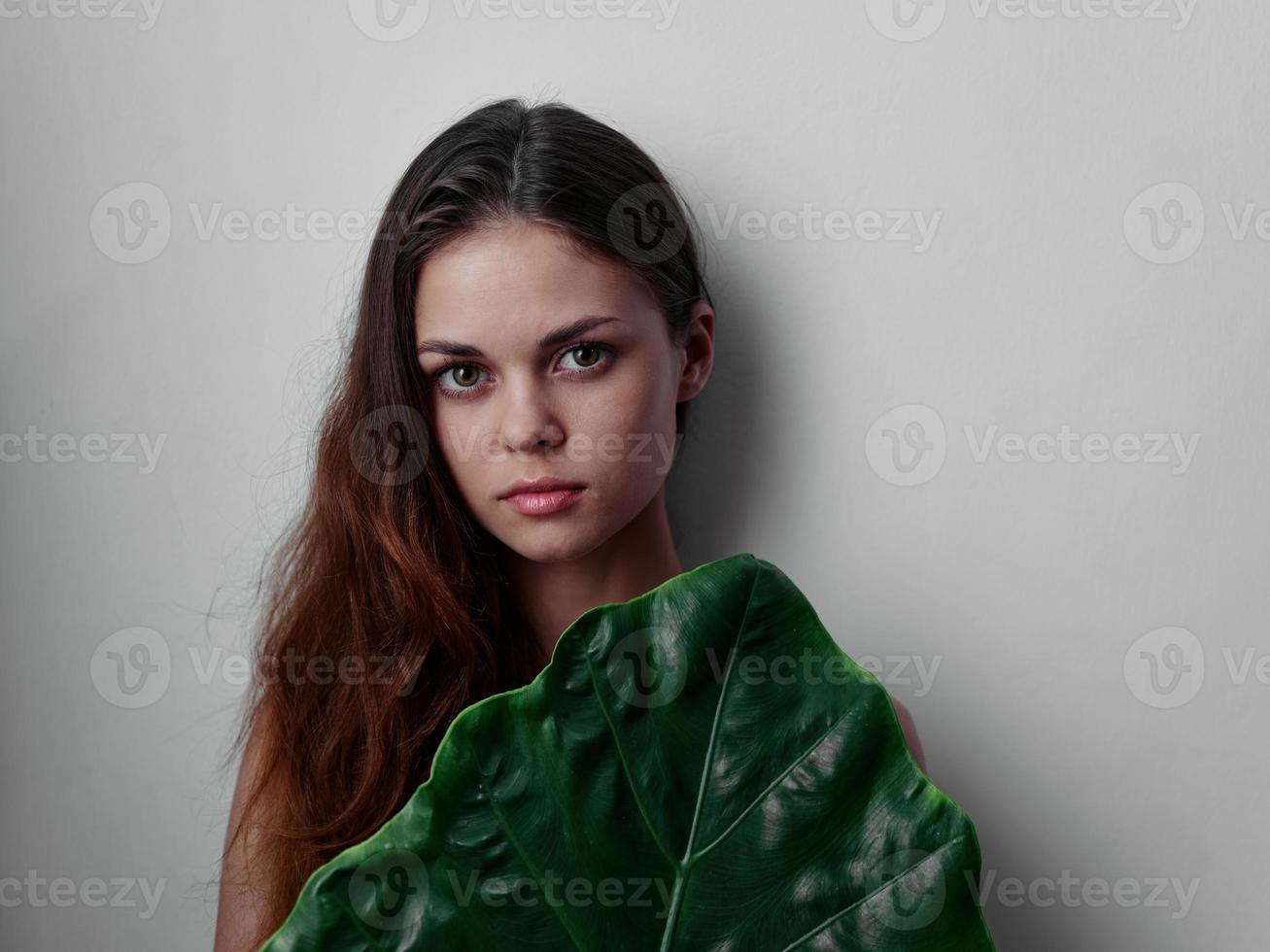 red-haired woman with bare shoulders hiding behind green studio leaf photo