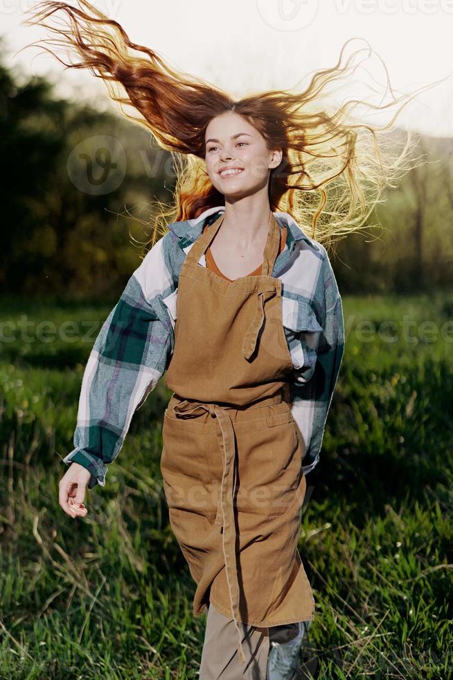 Woman walking on the grass in nature smiling in farm clothes with beautiful hair flying in the wind happy in the rays of summer sunset light photo