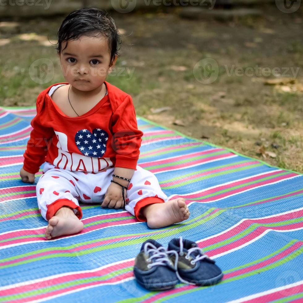 Cute little Indian infant sitting enjoying outdoor shoot at society park in Delhi, Cute baby boy sitting on colourful mat with grass around, Baby boy outdoor shoot photo