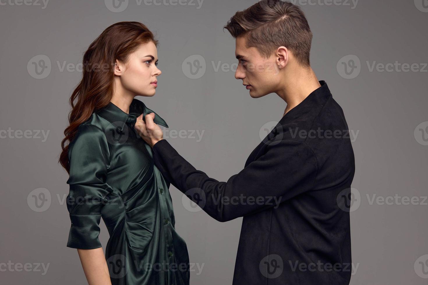 Aggressive man in a suit holds a woman by the collar of a dress on a gray background photo