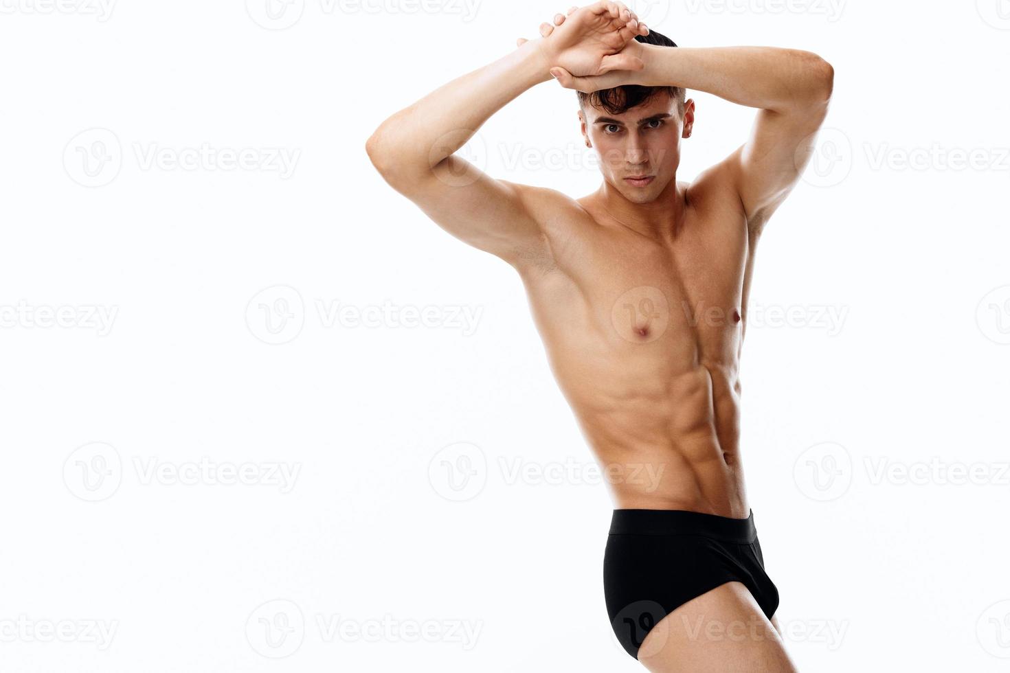 sexy guy with an athletic physique holds his hands near the face on a light background photo