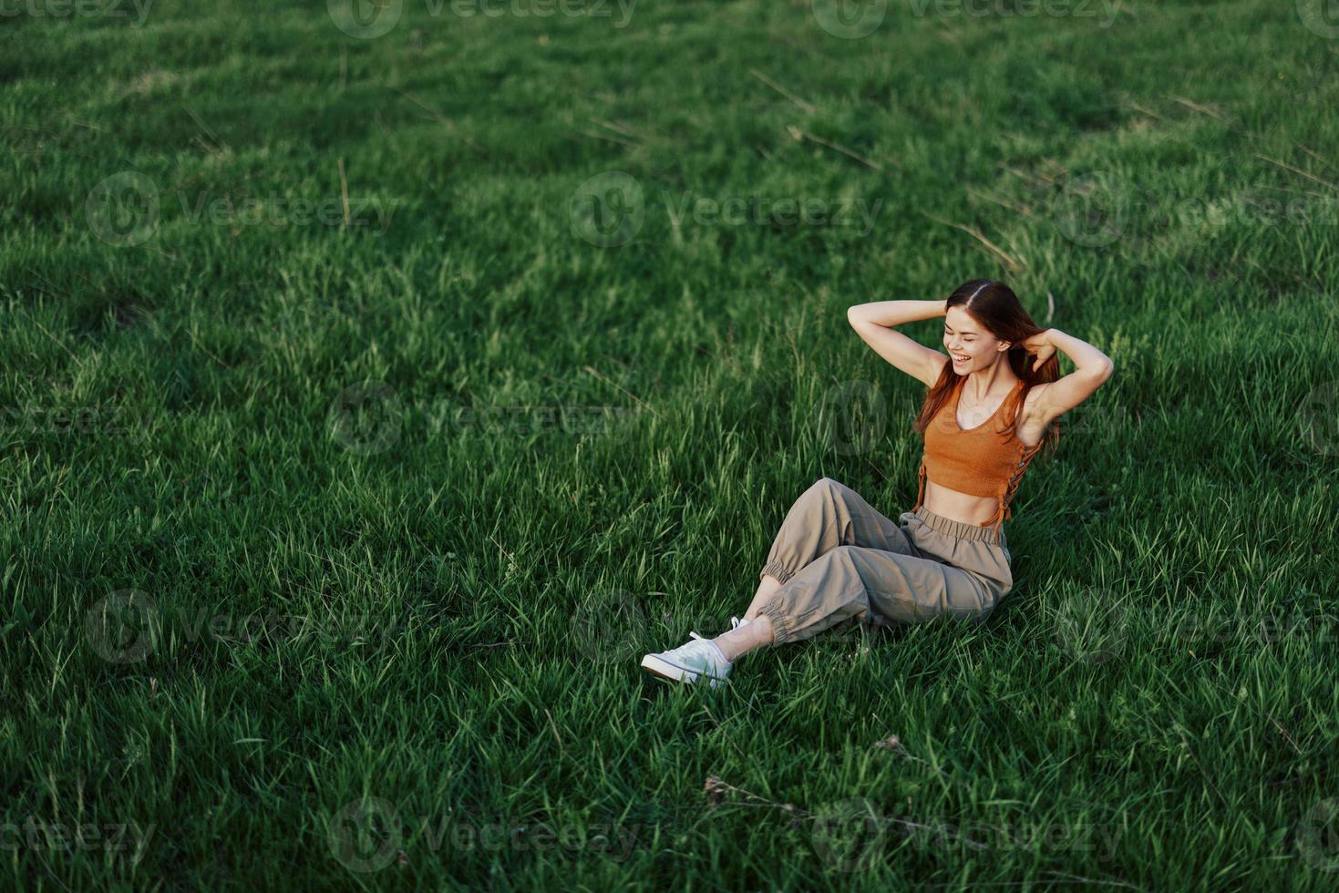 Young woman playing games in the park on the green grass spreading her arms and legs in different directions falling and smiling in the sunlight of summer, a lifestyle of life and youth photo