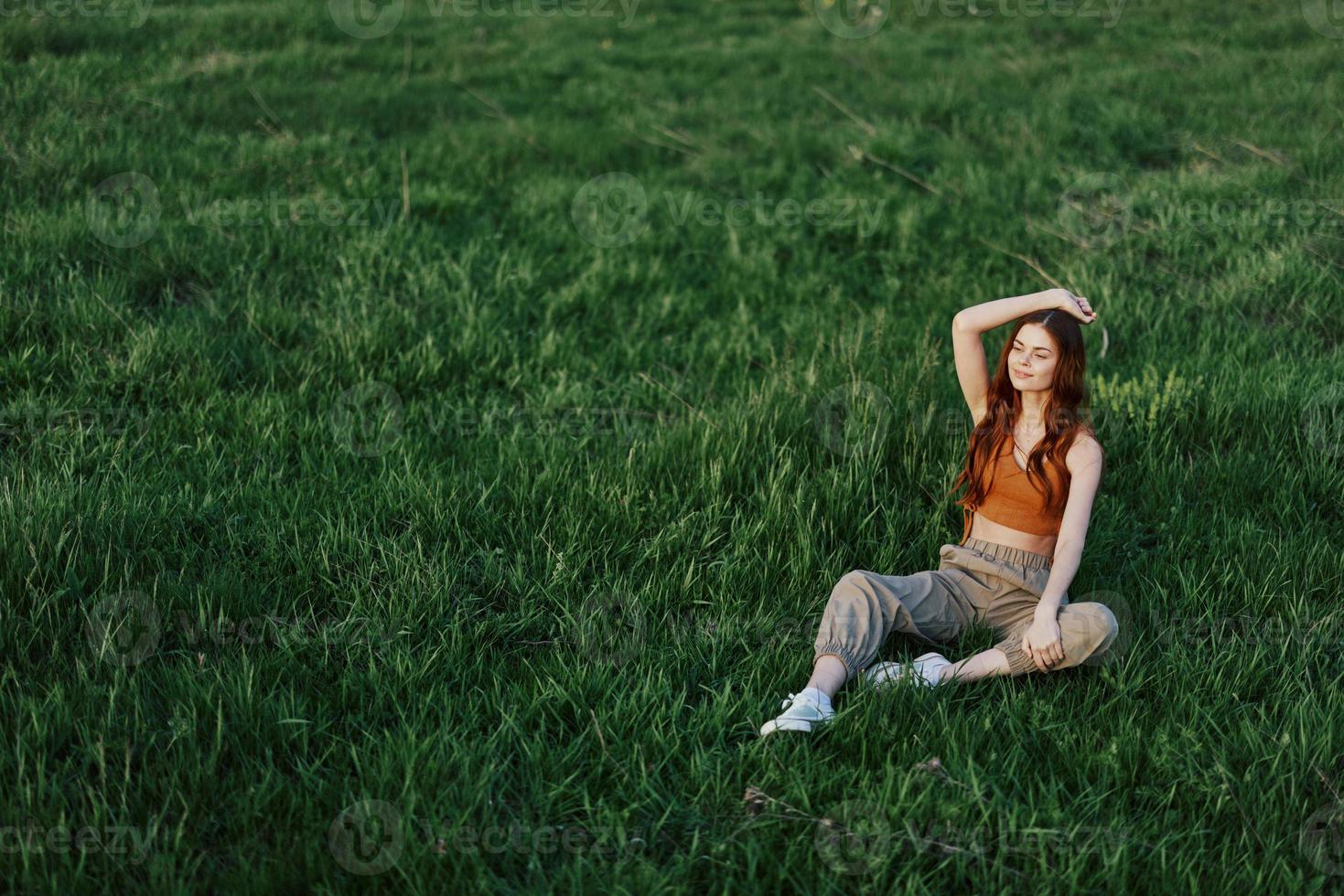 un niña en cómodo ropa se sentó en el césped después un caminar en el parque a meditar y descanso en el luz de sol foto