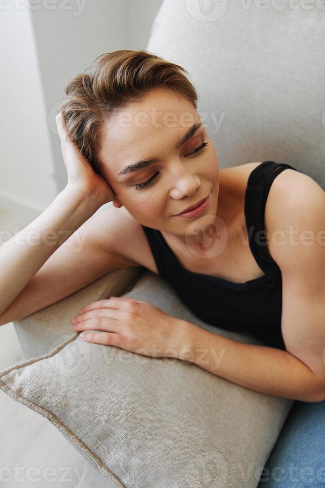 joven mujer con corto Corte de pelo pelo teniendo divertido a hogar en el sofá sonrisa y felicidad, vacaciones a hogar, natural posando sin filtros, gratis Copiar espacio foto