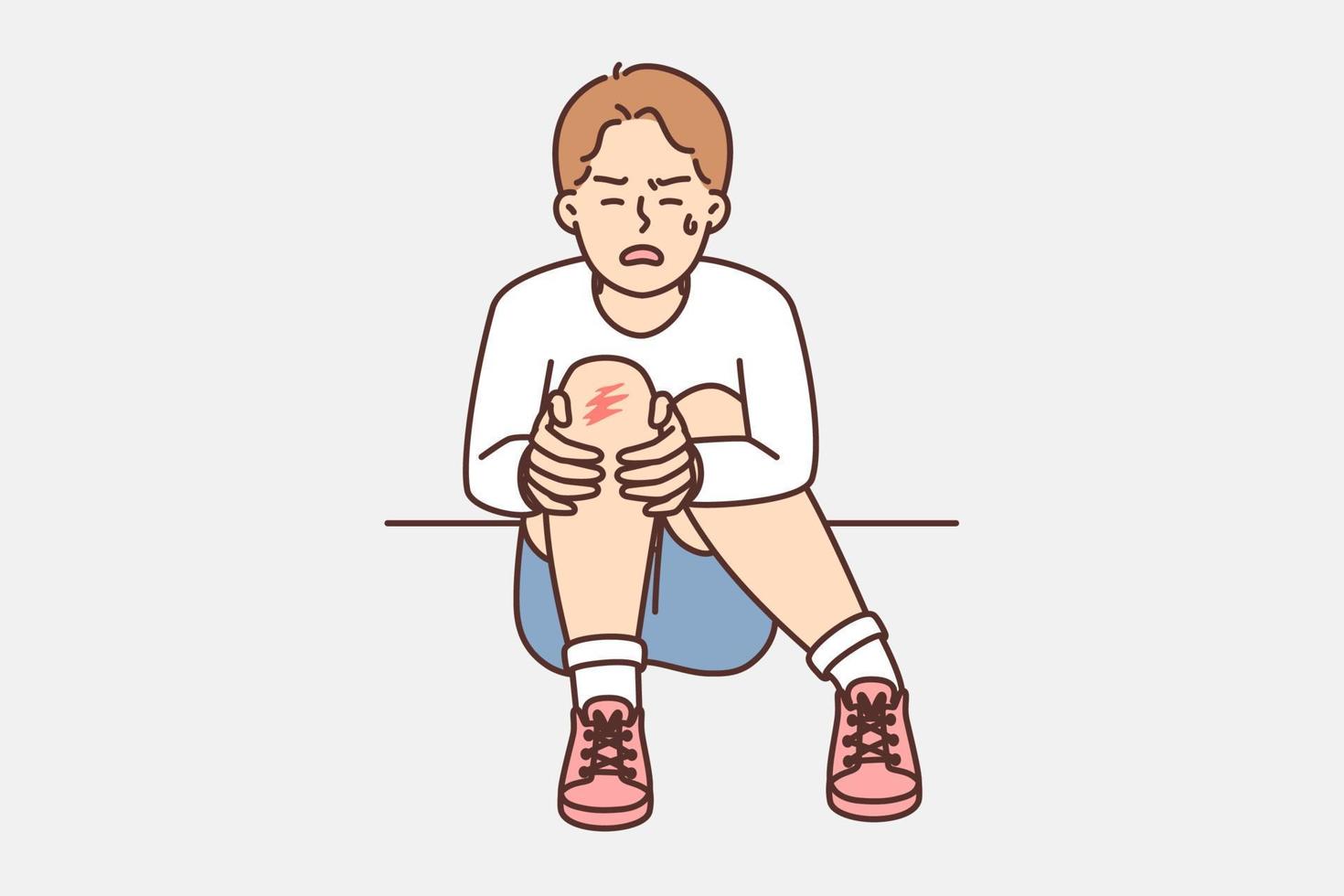 Crying teenager boy sits on ground and holds on to injury on knee after fall during walk. Unfortunate child was injured during sports activities or active games with friends vector