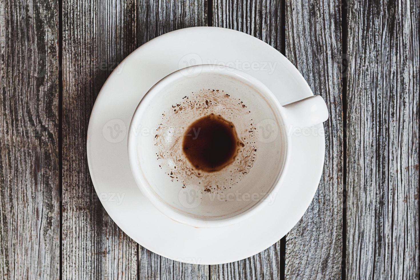 Empty cup with coffee leftovers on wooden table, top view photo