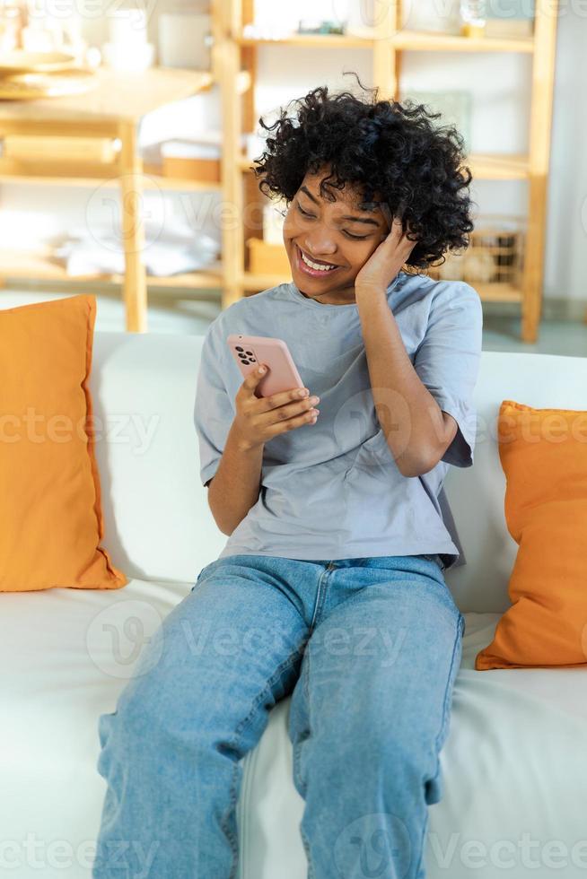 African girl holding smartphone touch screen typing scroll page at home. Woman with cell phone surfing internet using social media apps playing game. Shopping online Internet news cellphone addiction. photo