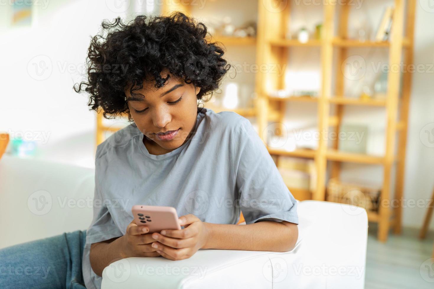 African girl holding smartphone touch screen typing scroll page at home. Woman with cell phone surfing internet using social media apps playing game. Shopping online Internet news cellphone addiction. photo