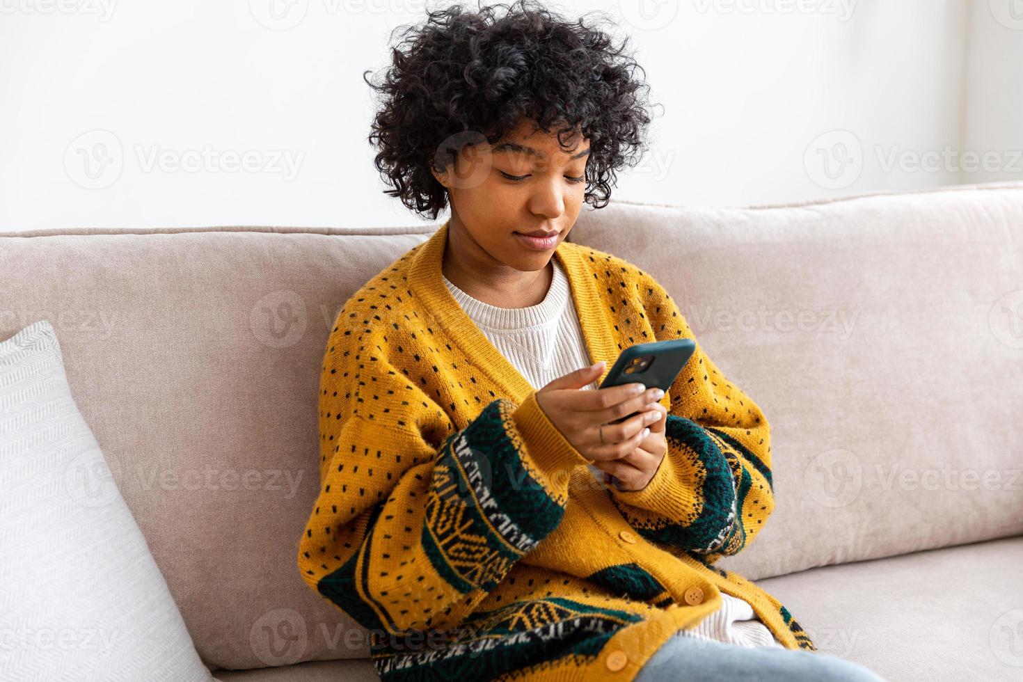 African girl holding smartphone touch screen typing scroll page at home. Woman with cell phone surfing internet using social media apps playing game. Shopping online Internet news cellphone addiction. photo