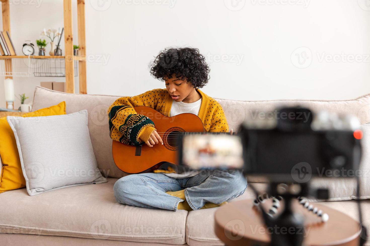 Blogger guitarist. African american girl blogger playing guitar talking to webcam recording vlog. Social media influencer woman streaming at home indoors. Music content creator broadcast tutorial. photo
