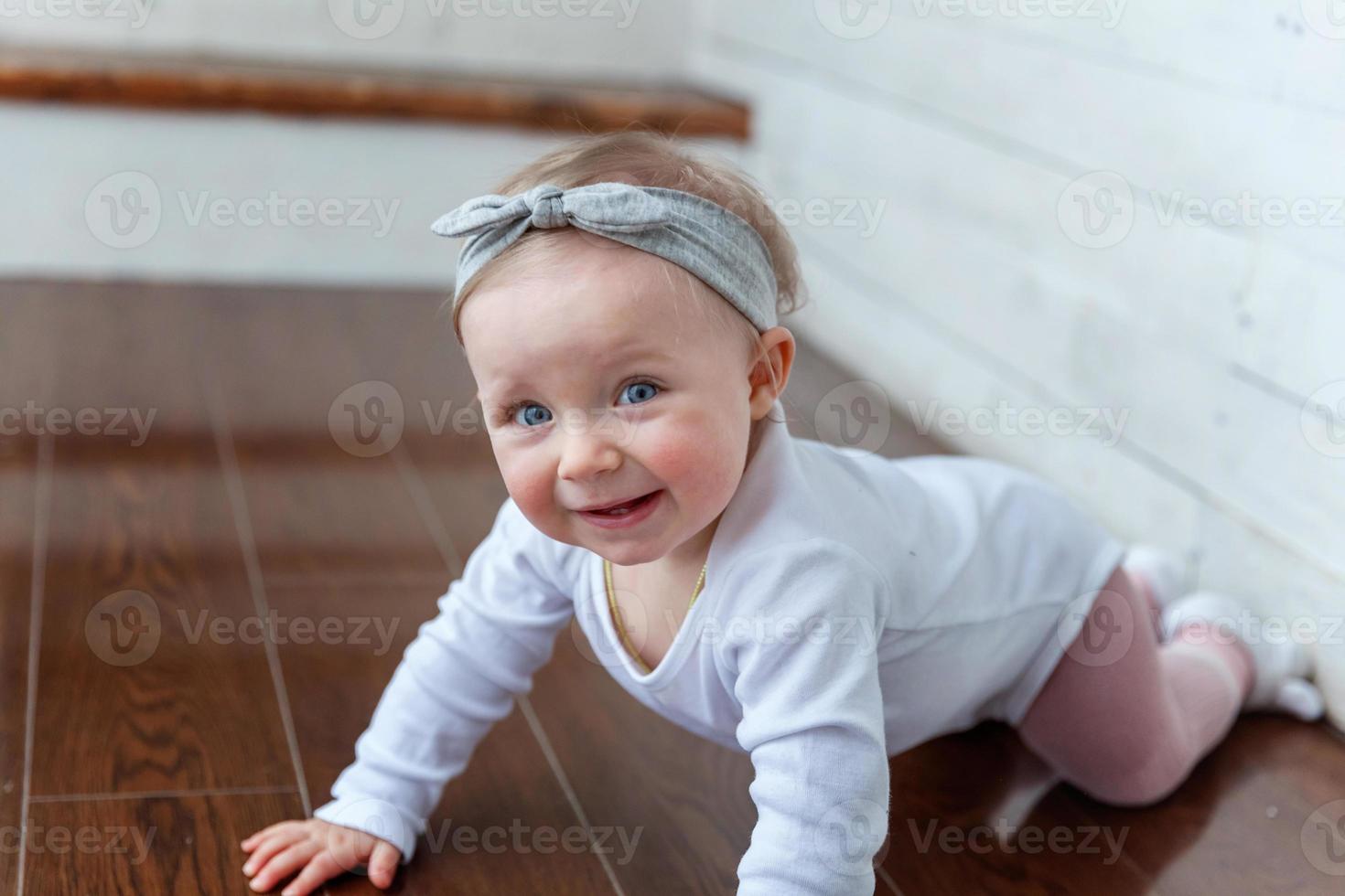 Little crawling baby girl one year old siting on floor in bright light living room near window smiling and laughing photo