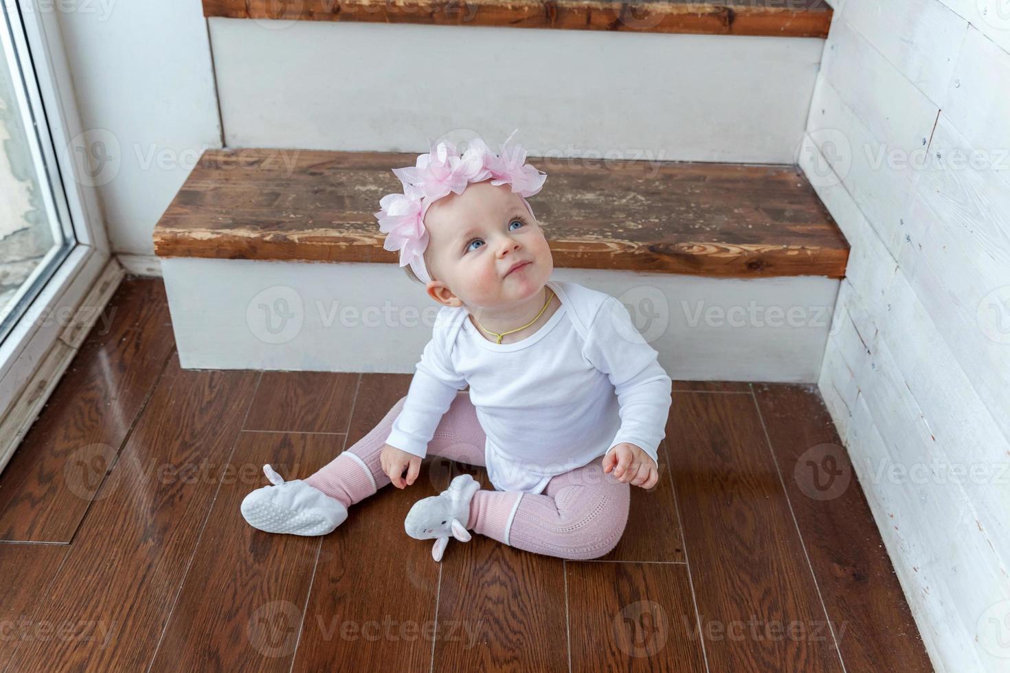 Little crawling baby girl one year old siting on floor in bright light living room near window smiling and laughing photo