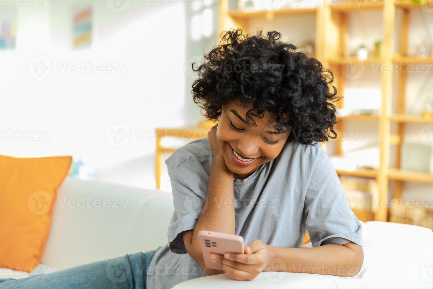 African girl holding smartphone touch screen typing scroll page at home. Woman with cell phone surfing internet using social media apps playing game. Shopping online Internet news cellphone addiction. photo