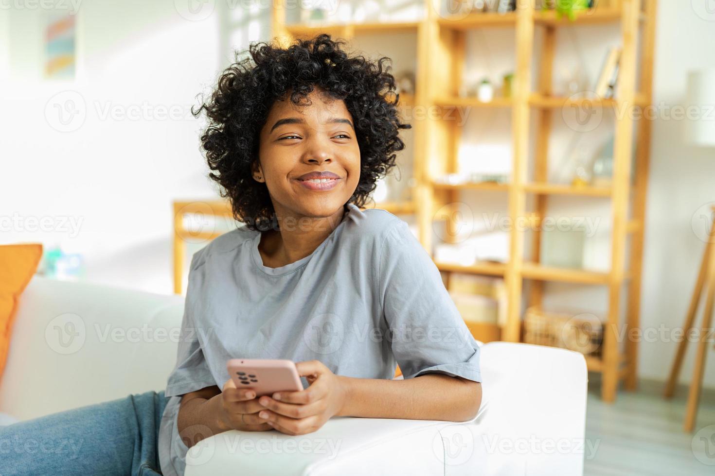 African girl holding smartphone touch screen typing scroll page at home. Woman with cell phone surfing internet using social media apps playing game. Shopping online Internet news cellphone addiction. photo