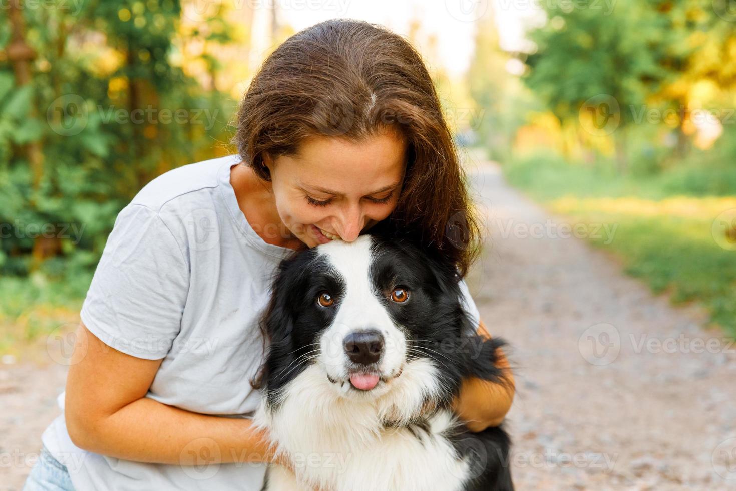 Smiling young attractive woman playing with cute puppy dog border collie on summer outdoor background. Girl holding embracing hugging dog friend. Pet care and animals concept. photo