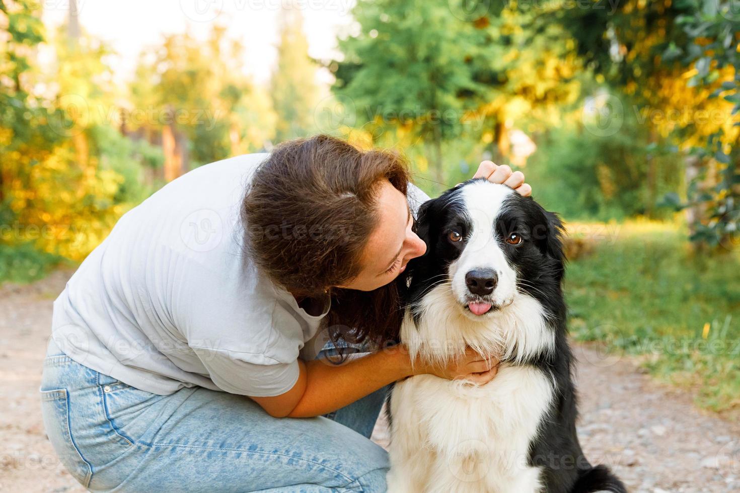 Young attractive woman playing with cute puppy dog border collie on summer outdoor background. Girl kissing holding embracing hugging dog friend. Pet care and animals concept. photo